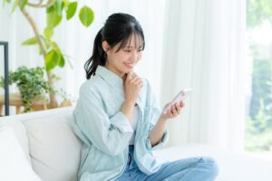 自宅のソファに座ってスマホを見ている日本人女性