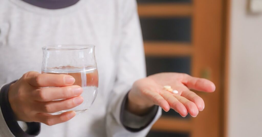 右手で水の入ったグラスを持ち左手の手の平に錠剤を乗せている女性