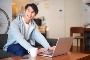 自宅でノートパソコンを操作する若い日本人男性
